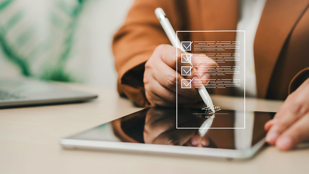 Person signs an electronic form on a tablet with a digital checklist overlay.