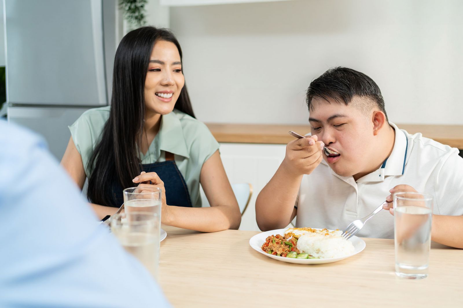 Young man with Down syndrome cooking in contemporary kitchen with female assistant